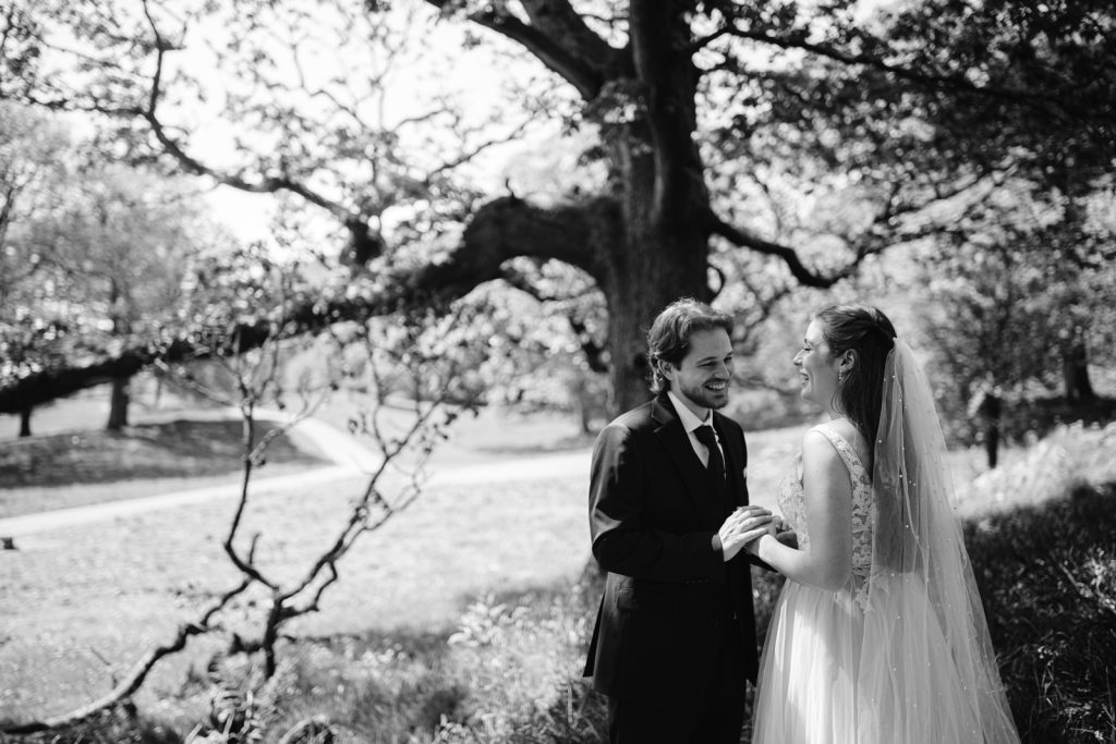 A bride and groom eloping in a picturesque wooded area near a lakeside hotel.