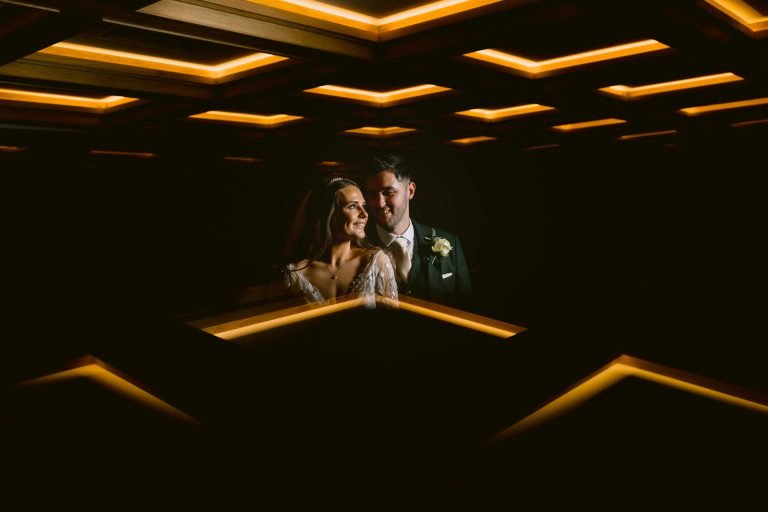 A Ruleholme couple, wrapped in Winter fleece, standing in a dark room illuminated by lights.