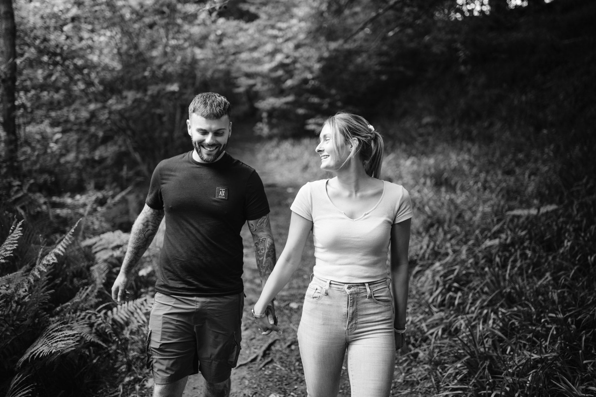 A black and white portrait session of a couple walking through the woods.