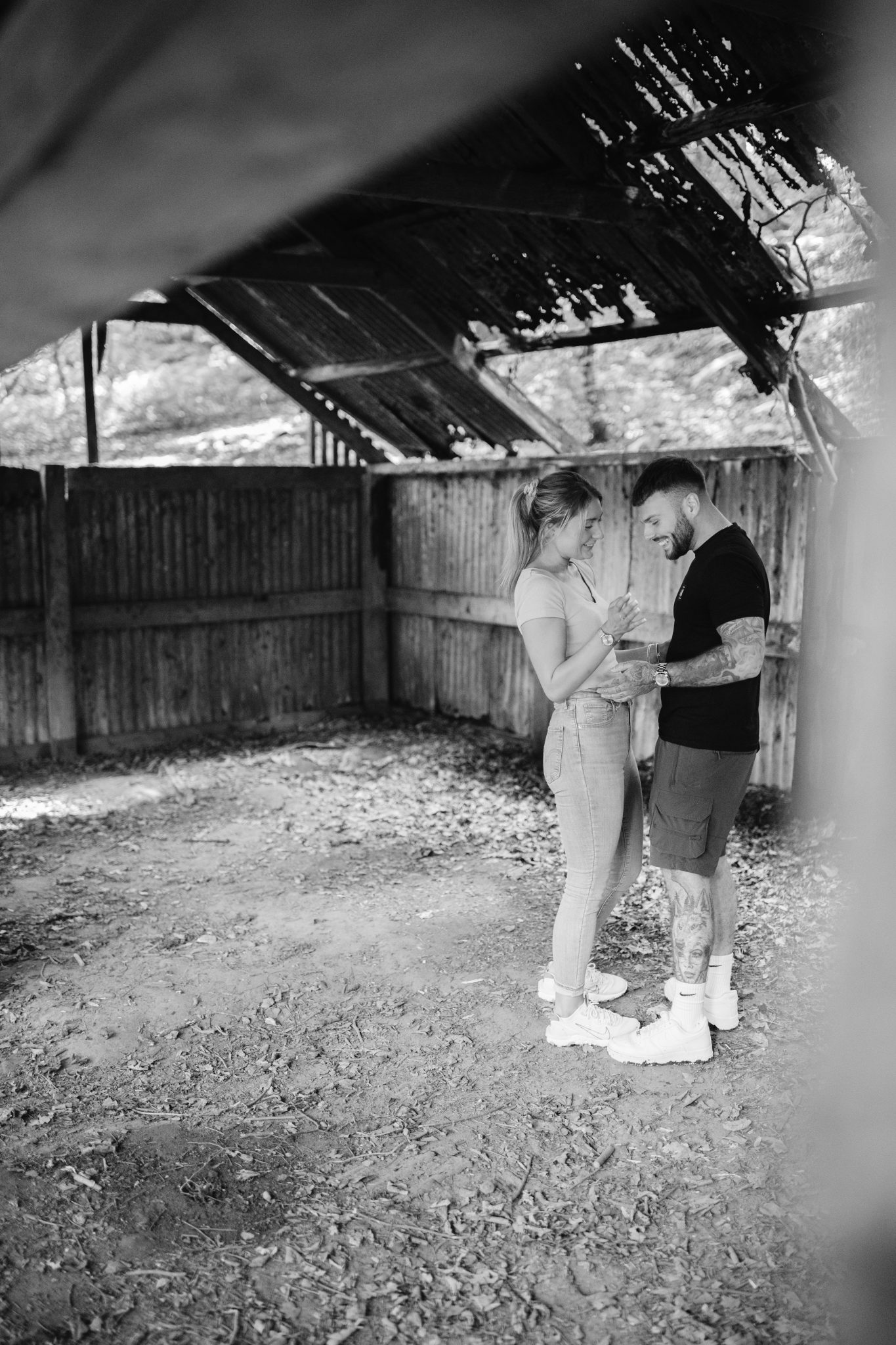 A black and white photo of a couple standing in a barn, captured during their portrait session.