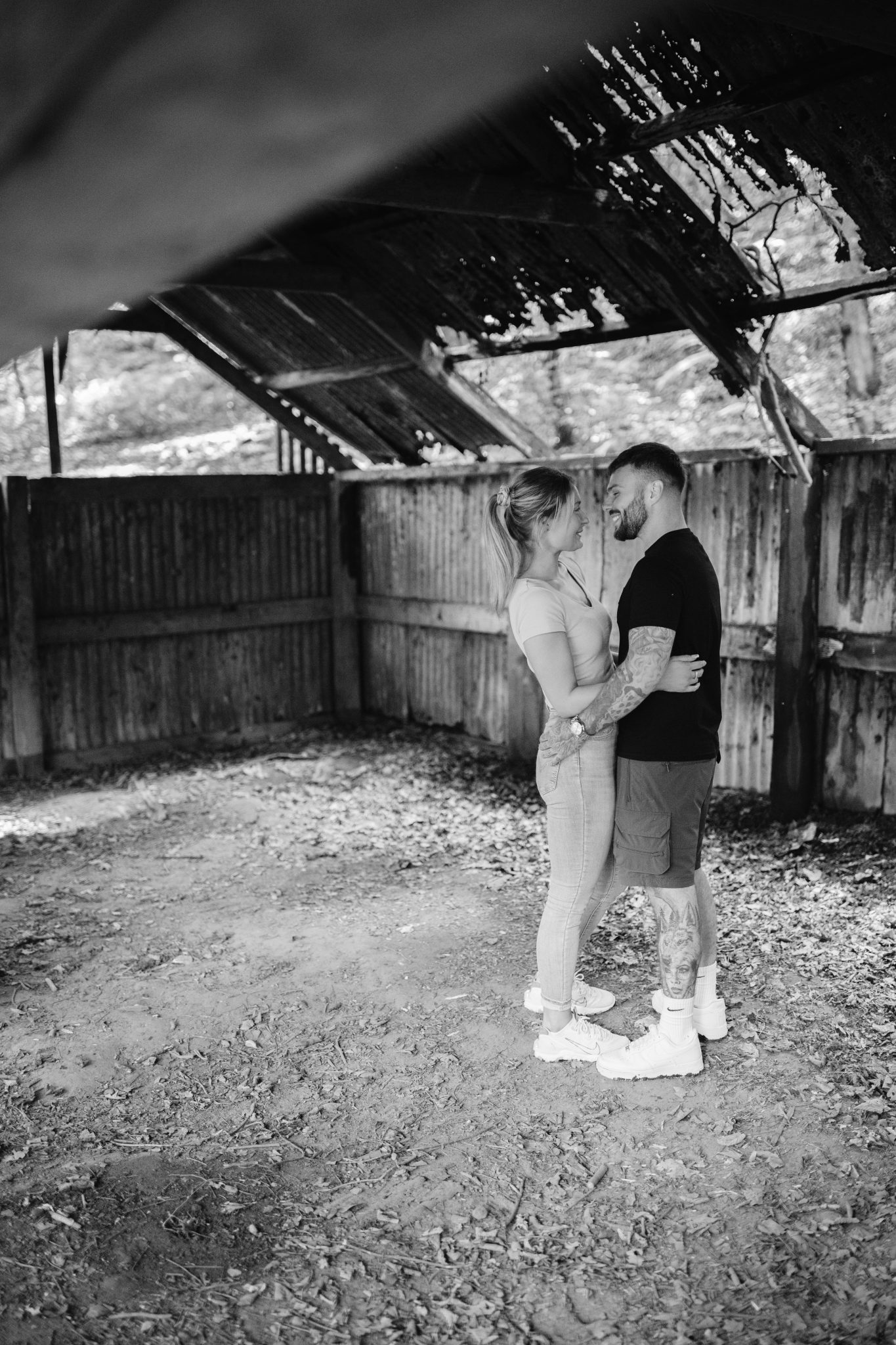 A black and white photo of a couple embracing in a wood barn.