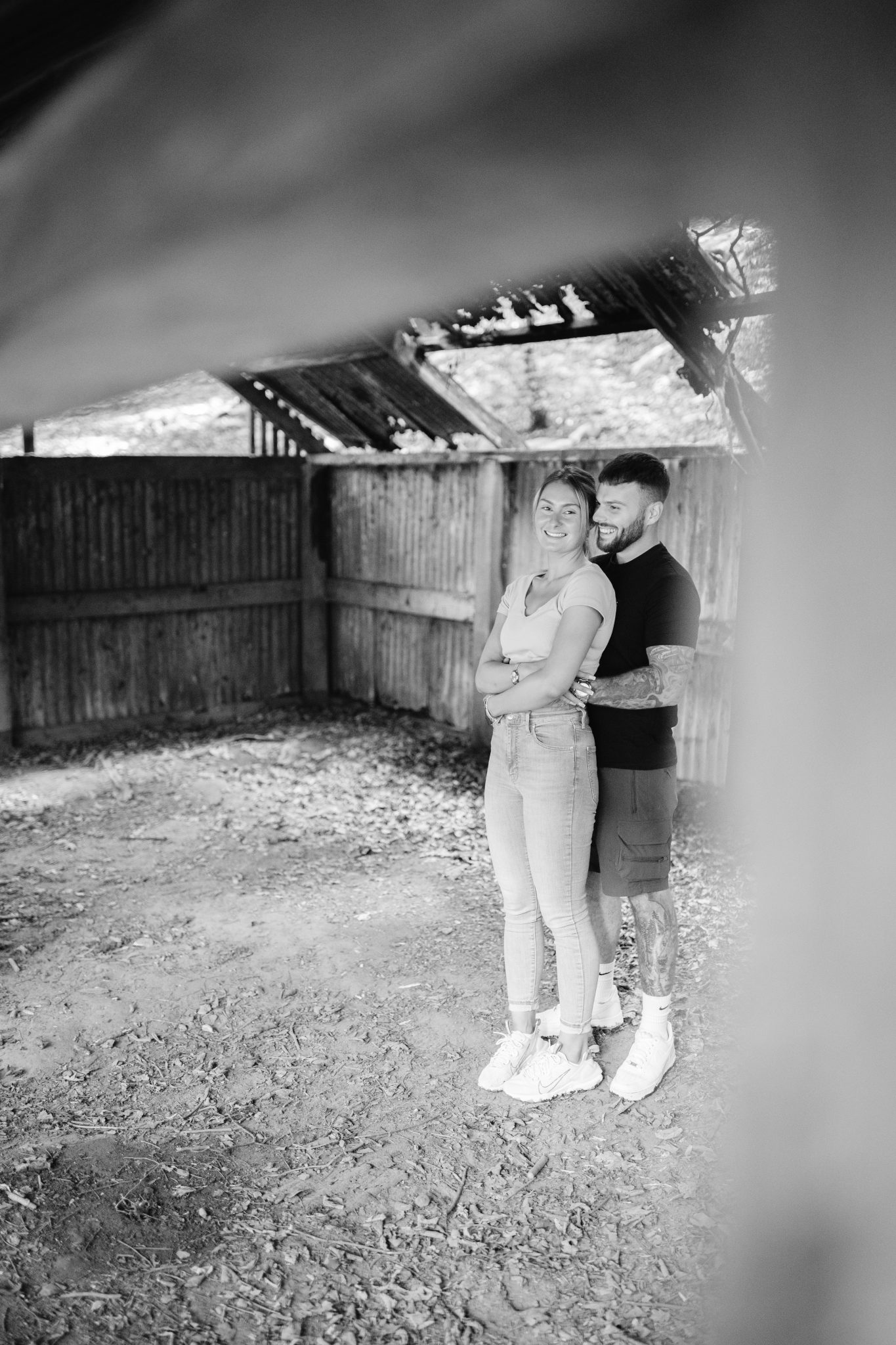 A black and white photo of a couple embracing in a barn during their portrait session.