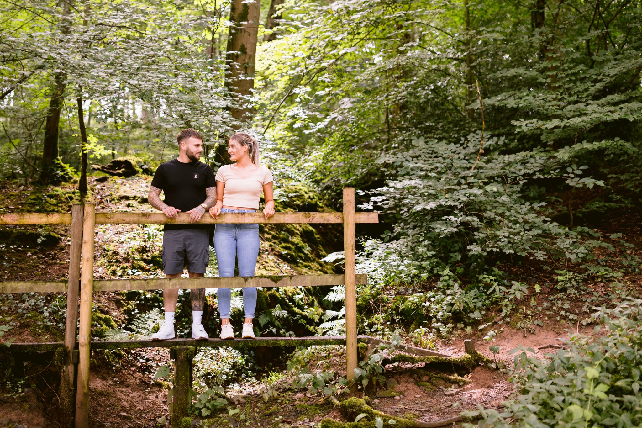 A couple enjoying a romantic portrait session on a wooden bridge in the woods.