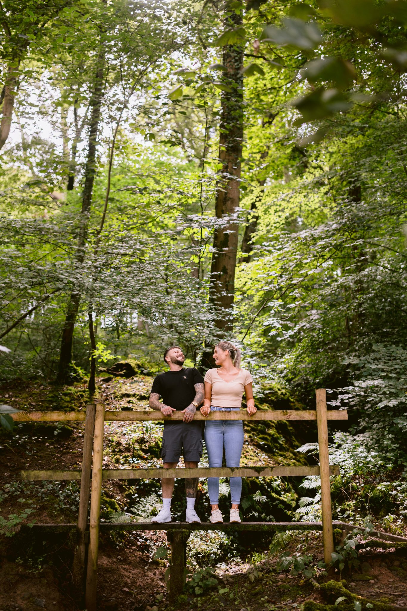 A couple standing on a wooden bridge in the woods during a portrait session.