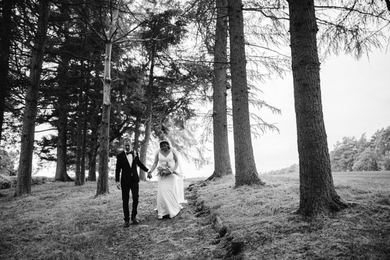 Black and white photo of a bride and groom at a Gretna Hall wedding, walking through the woods.