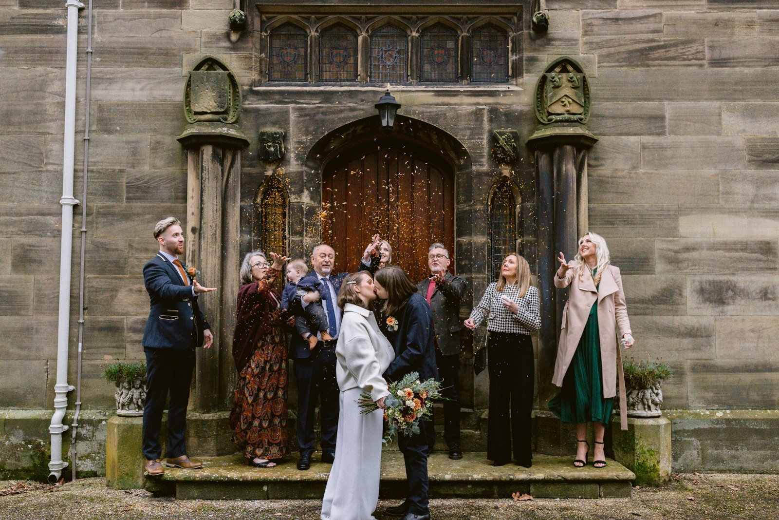 A group of bridesmaids and groomsmen posing in front of Lady Gillford's house, a historic old building during a winter wedding celebration.
