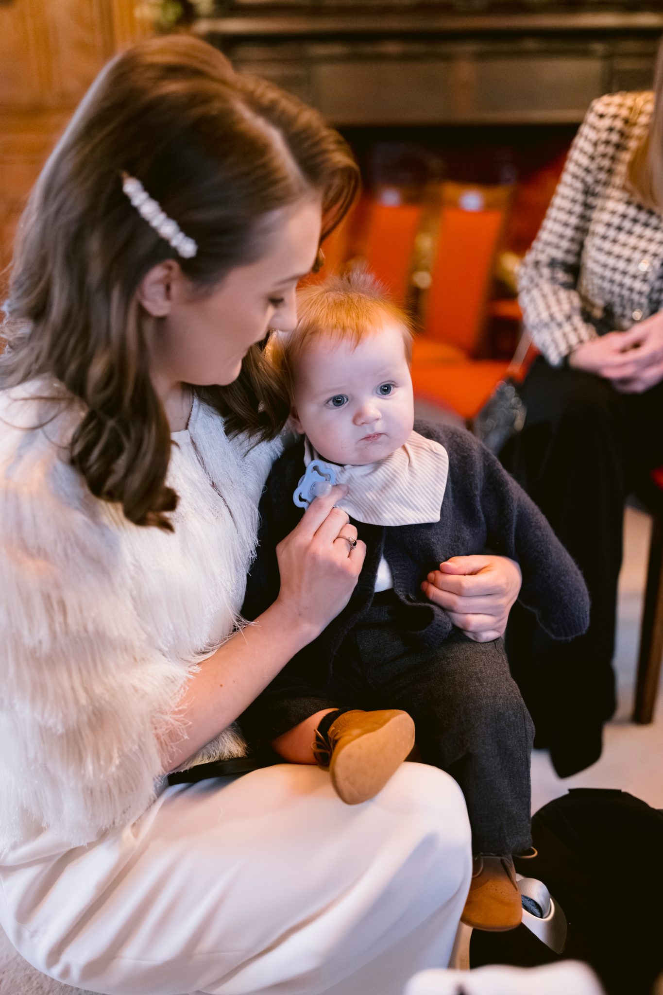 A lady is holding a baby in her lap at a winter wedding at Lady Gillford's house.