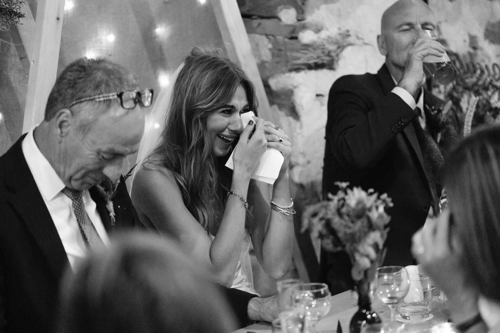 A woman holding a napkin and smiling while a man is singing at a summer wedding.