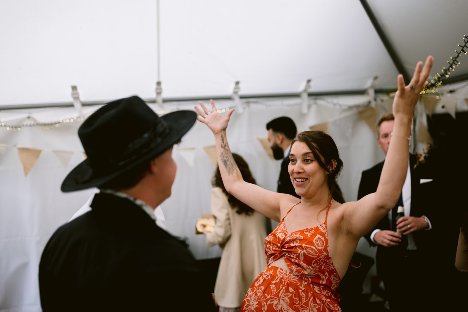 A woman in a red dress, captured at Yew Tree Farm, joyfully with her arms raised during a summer wedding ceremony.