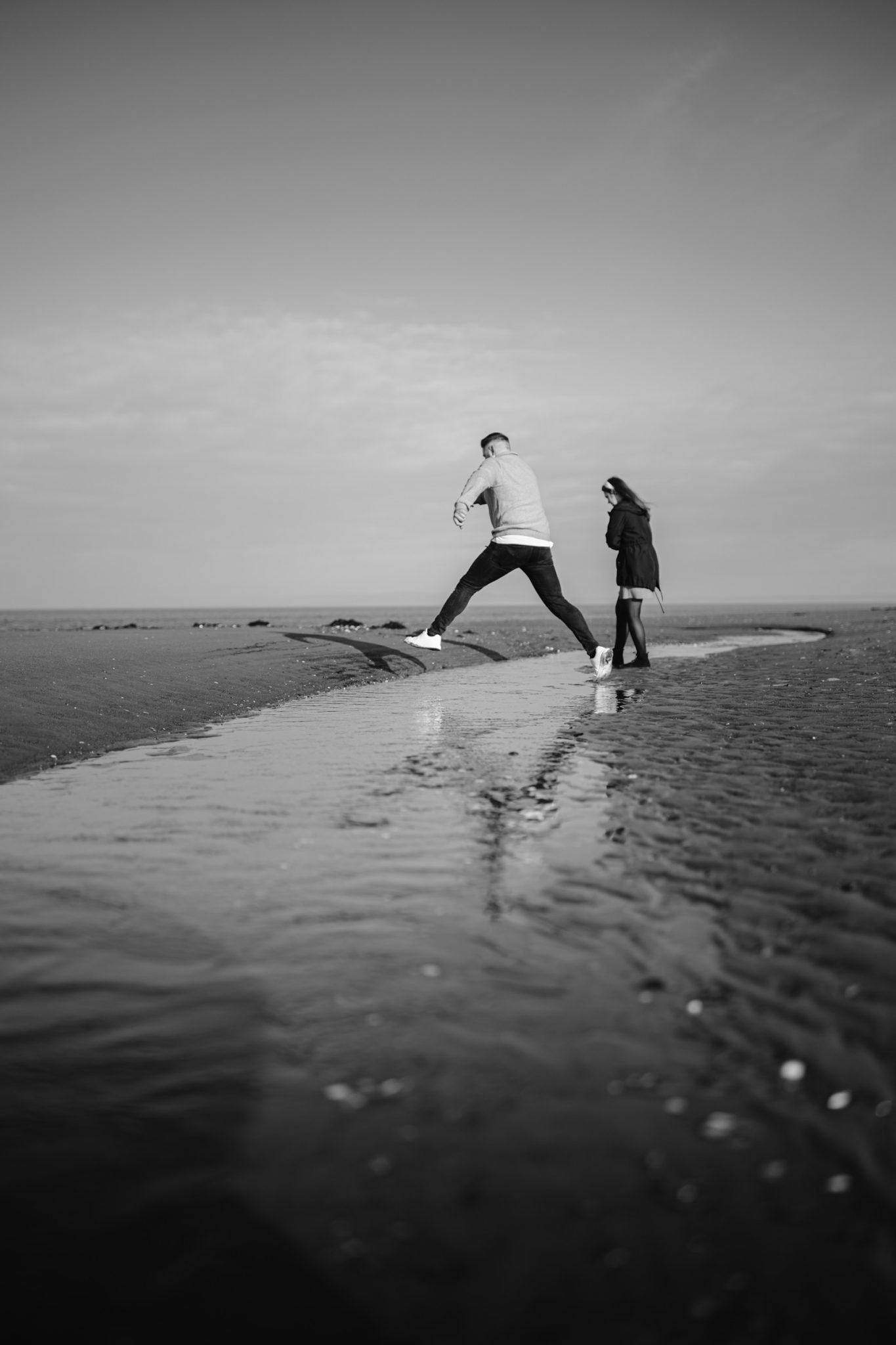 Two people walking along a shallow water stream by the lake, captured in black and white during their Portrait Session.