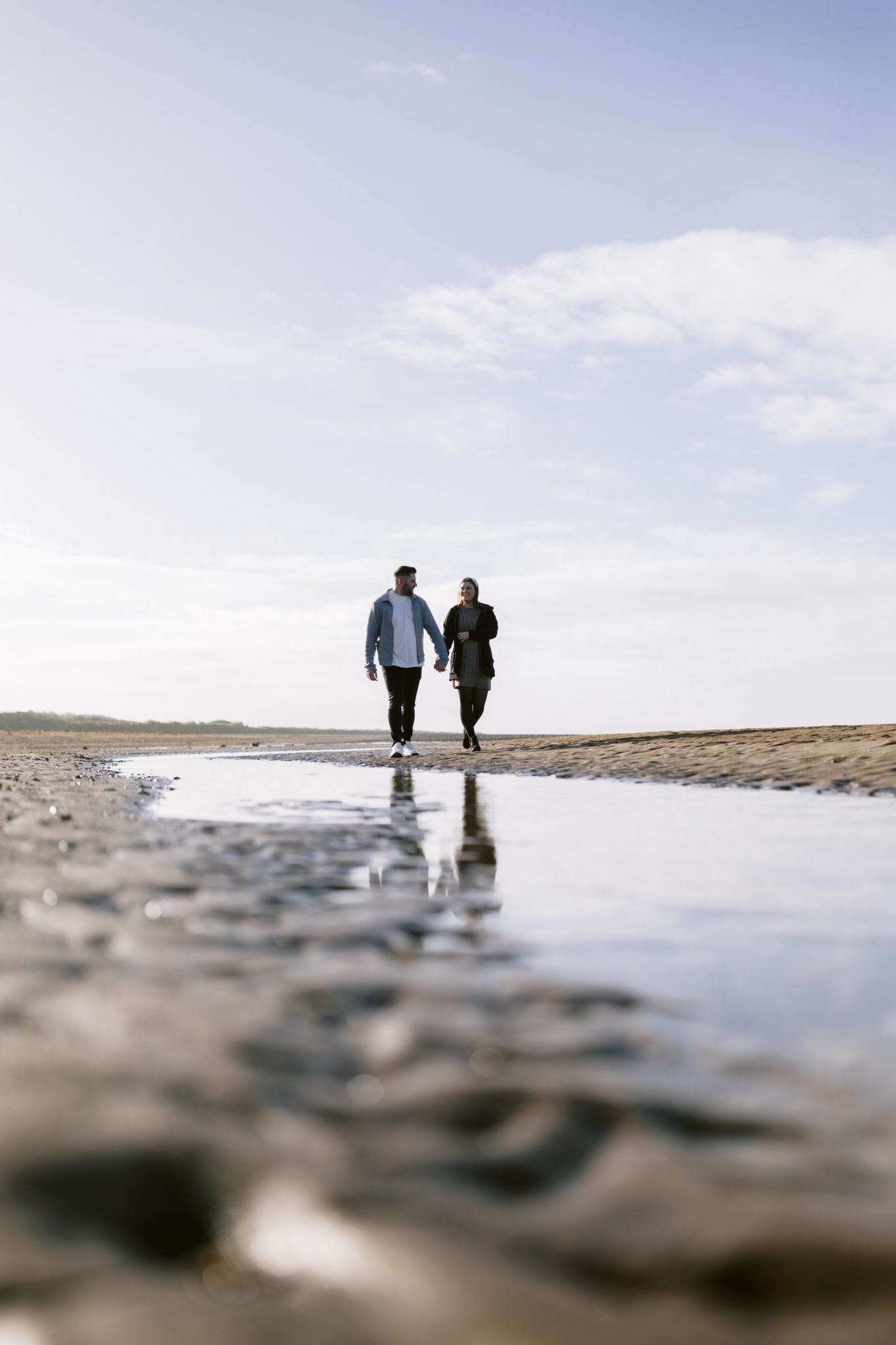 Two people walking side by side on a lake beach with reflective wet sand underfoot during their Portrait Session.