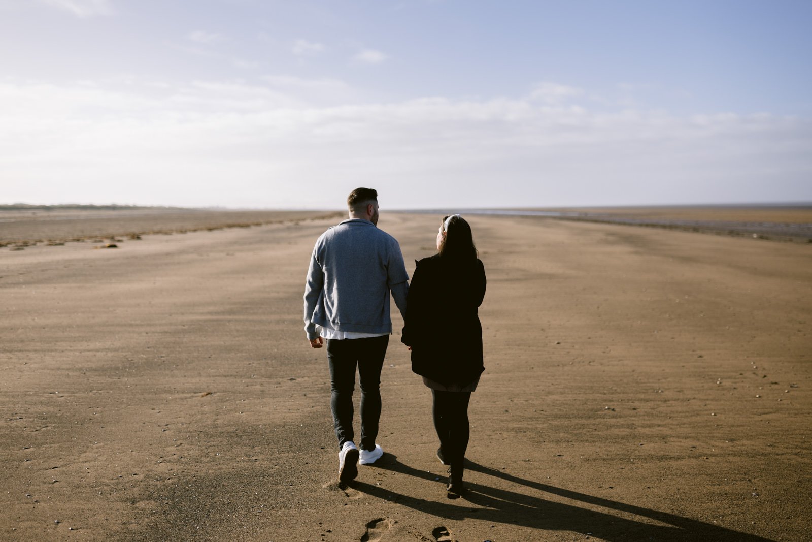 Two people enjoying a couple's portrait session together on a vast, sandy beach beside a serene river.