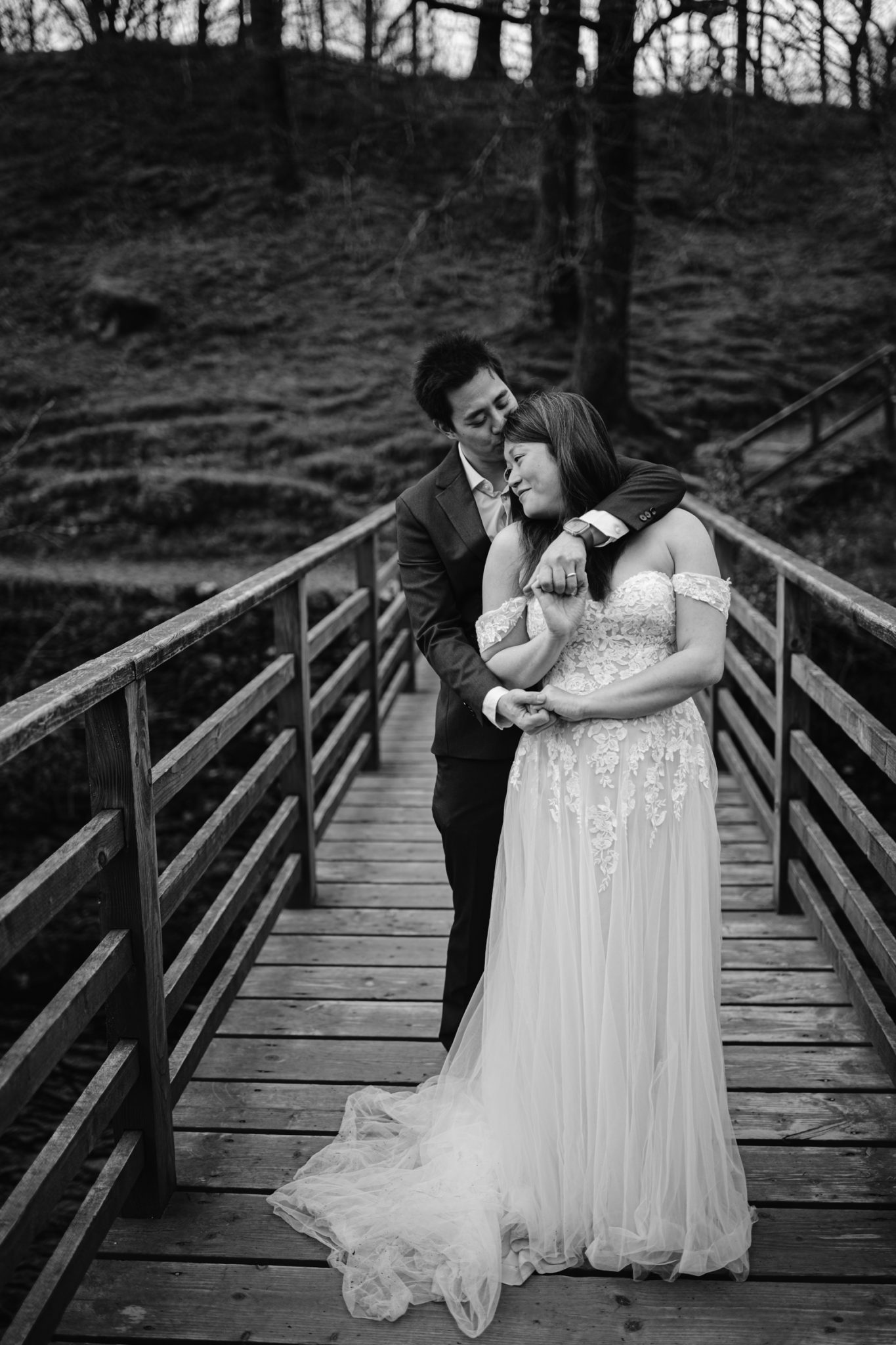 A couple celebrating their wedding anniversary sharing an intimate moment on a wooden bridge.