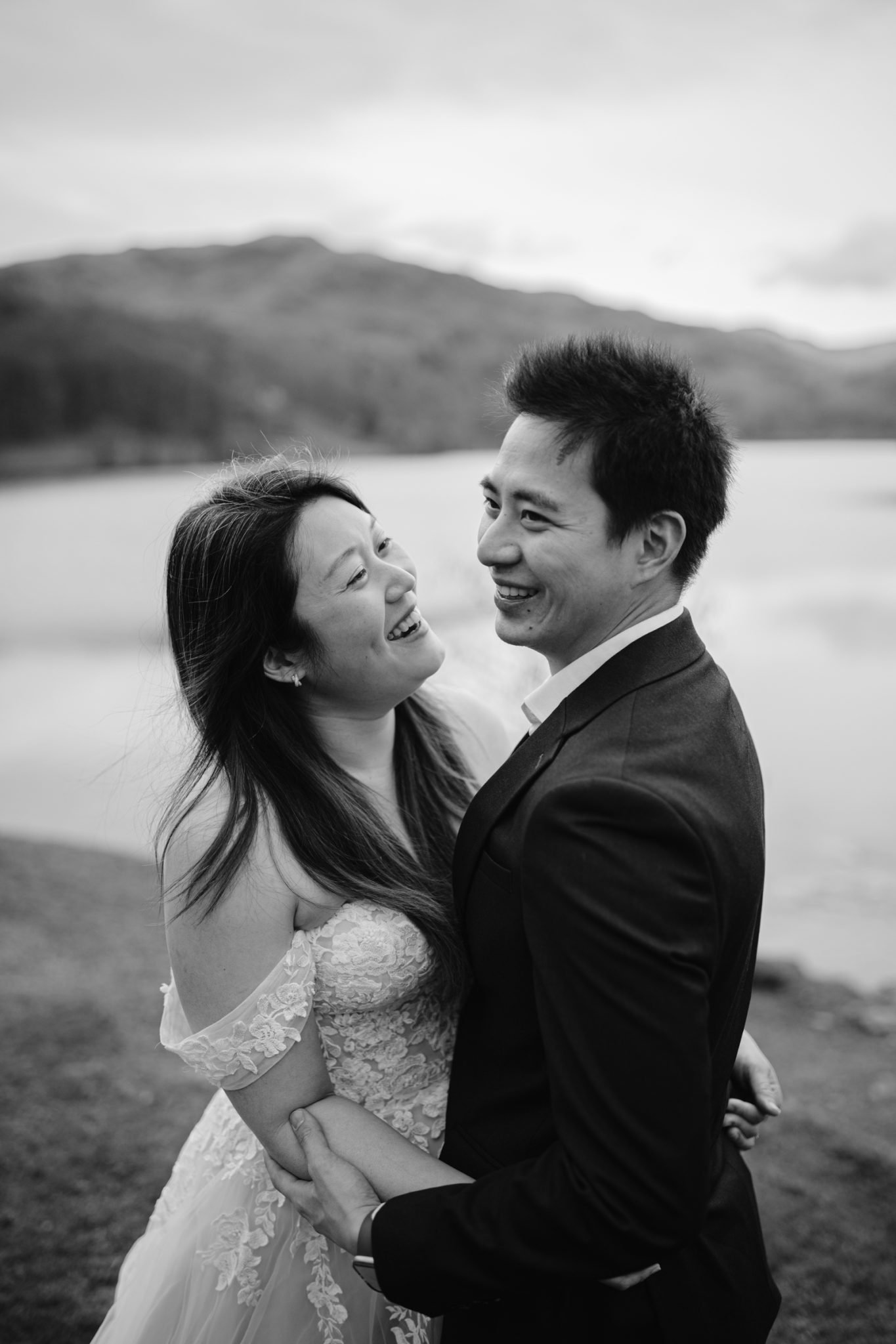 A joyful bride and groom sharing a moment by a lakeside with mountains in the background, celebrating their wedding anniversary.