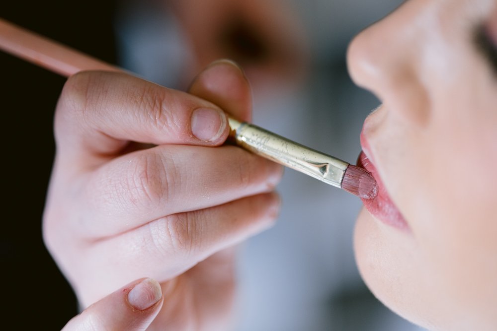 Close-up of a hand applying pink lipstick to someone's lips using a brush, perfect for that fun wedding look.