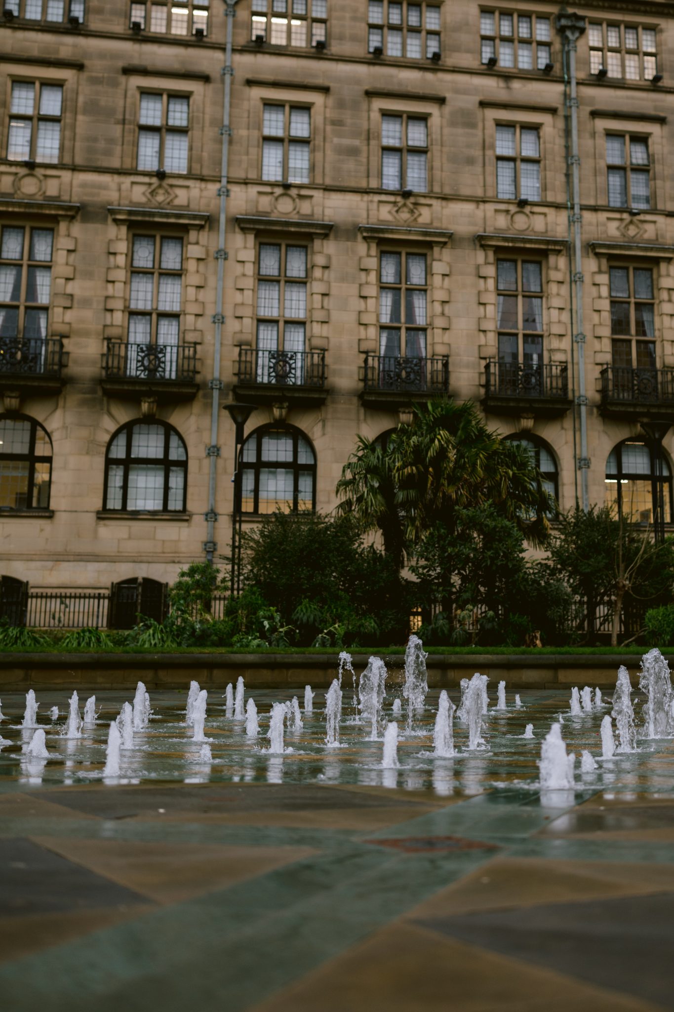 A view of a water fountain with multiple jets graces the front of an old stone building, reminiscent of the charm seen at Sheffield Registry Office Weddings, featuring several windows and balconies.