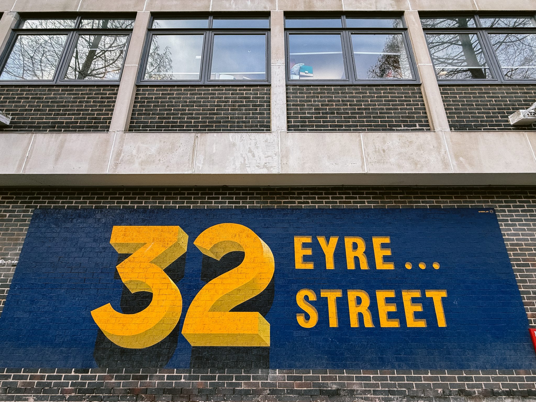 The brick facade at 32 Eyre Street features large yellow text on a blue background, evoking the charm of a Hidden River Wedding, nestled below a row of windows.