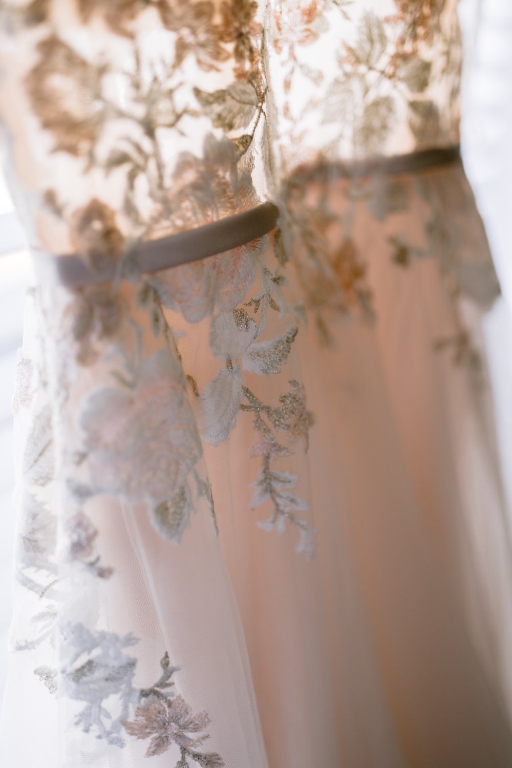 Close-up of a sheer fabric with floral embroidery in light colors, featuring intricate leaf and flower patterns.