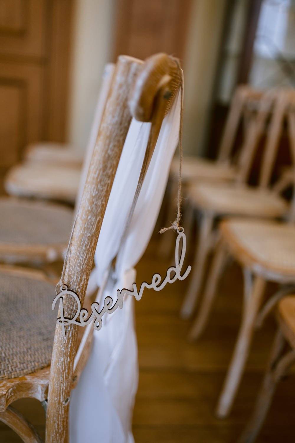 Wooden chair with a fabric sash and a "Reserved" sign hanging on the back, set on a wooden floor.