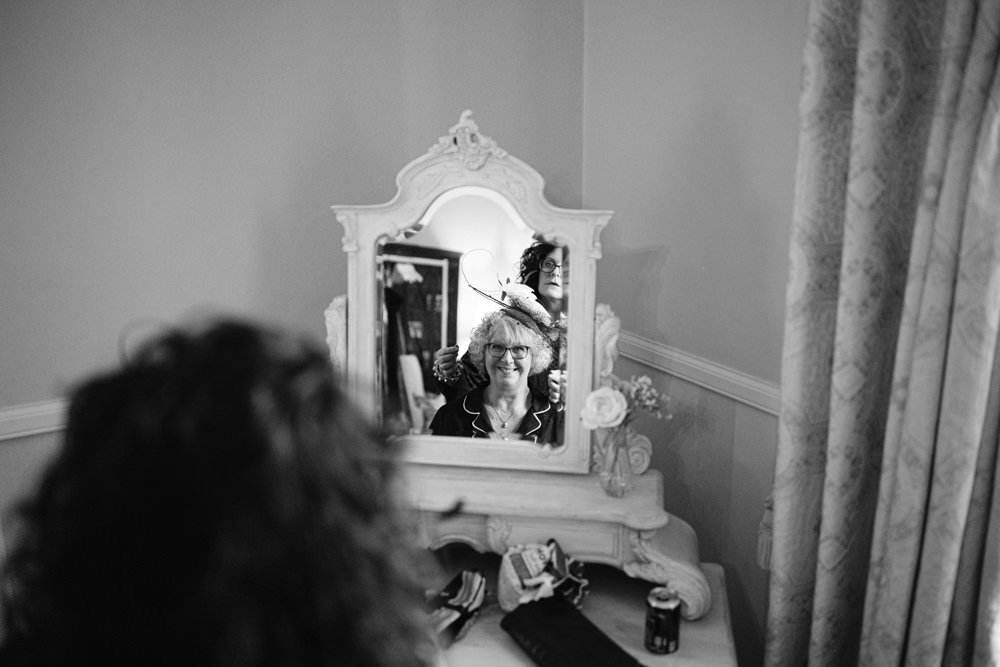 A woman smiling in front of a mirror while having her hair styled by another person in a room with a decorative vanity.