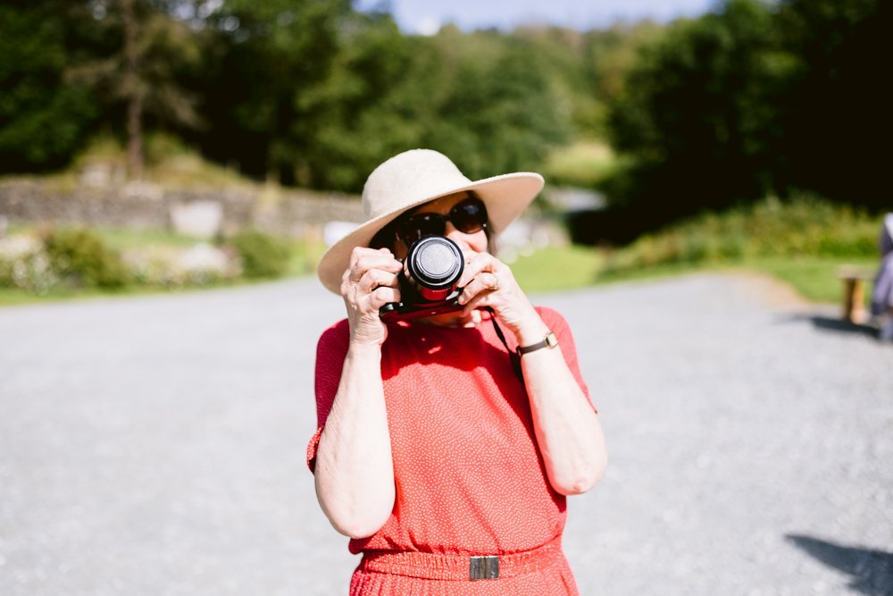 Person in a red outfit and sun hat using a camera outdoors in a sunny setting.