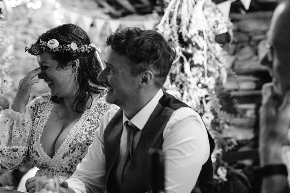 A woman wearing a floral headband laughs beside a man in a suit at a festive indoor gathering.