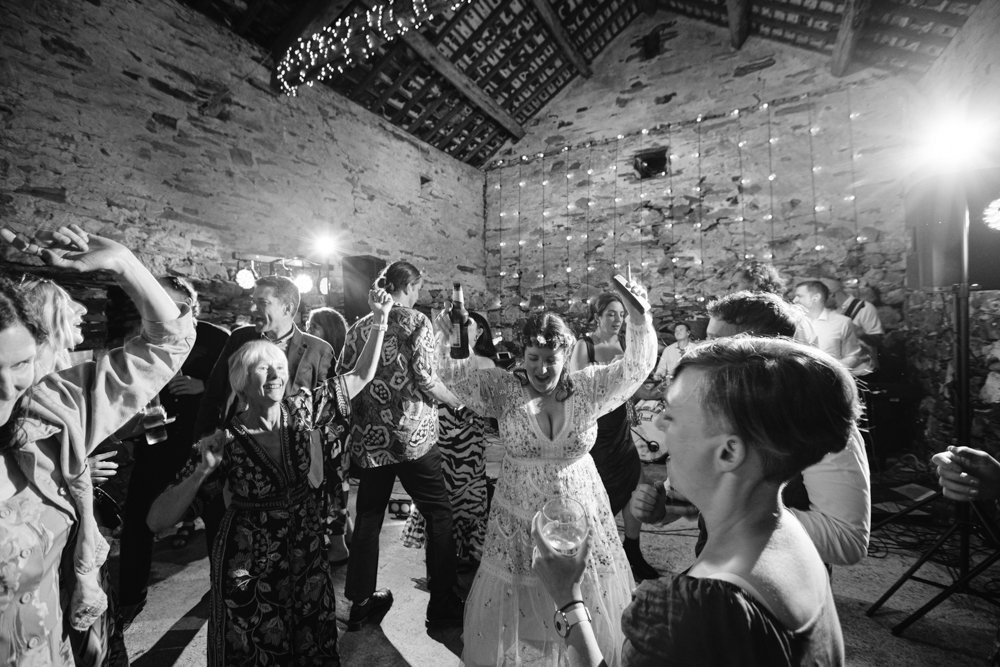People dancing energetically at an indoor event, surrounded by stone walls and hanging lights, in a festive atmosphere.