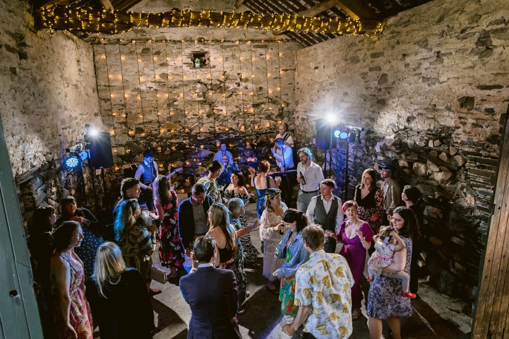 People dancing in a rustic venue with stone walls and string lights overhead.