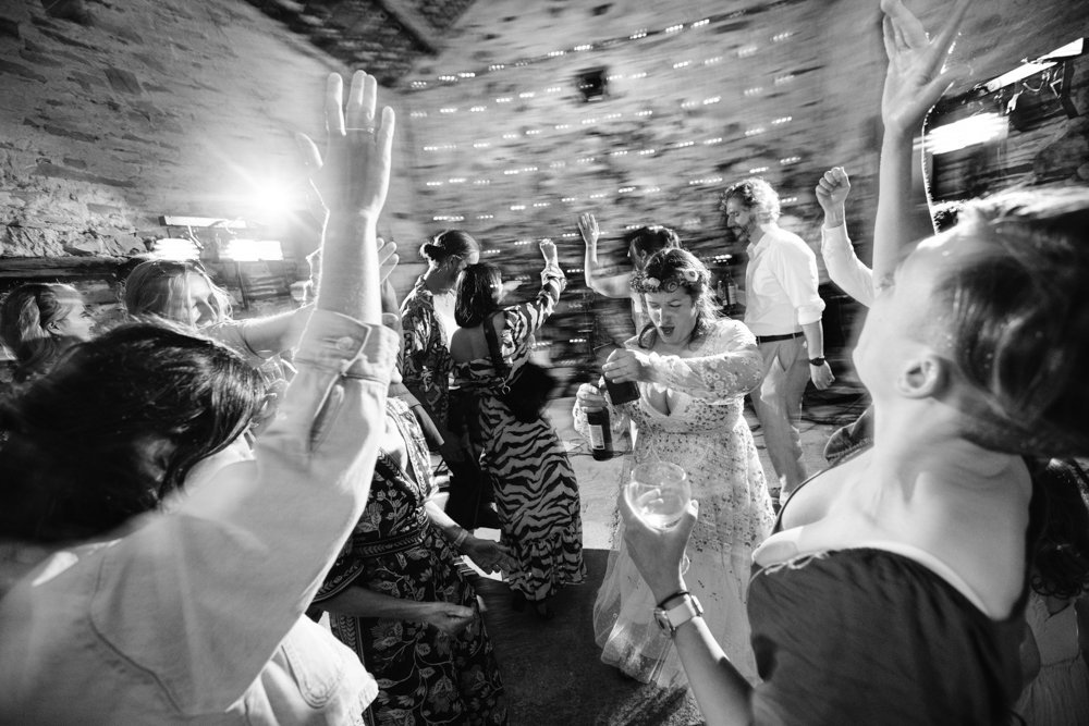 A lively group of people dancing at an indoor party, with some holding drinks and raising their hands in celebration.
