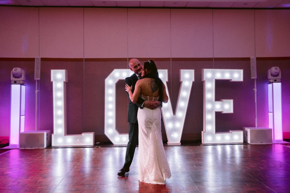 A couple dances gracefully on the wooden floor of Lady Gilford’s House, in front of large illuminated letters spelling "LOVE.