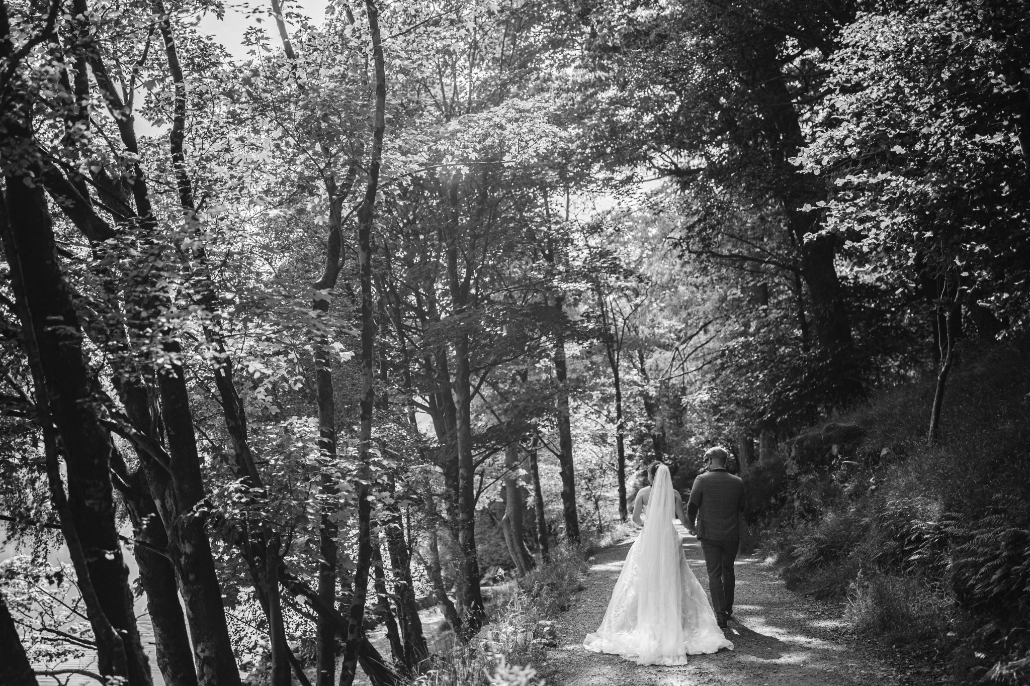 Bride and groom walking down a tree-lined path in a forested area.