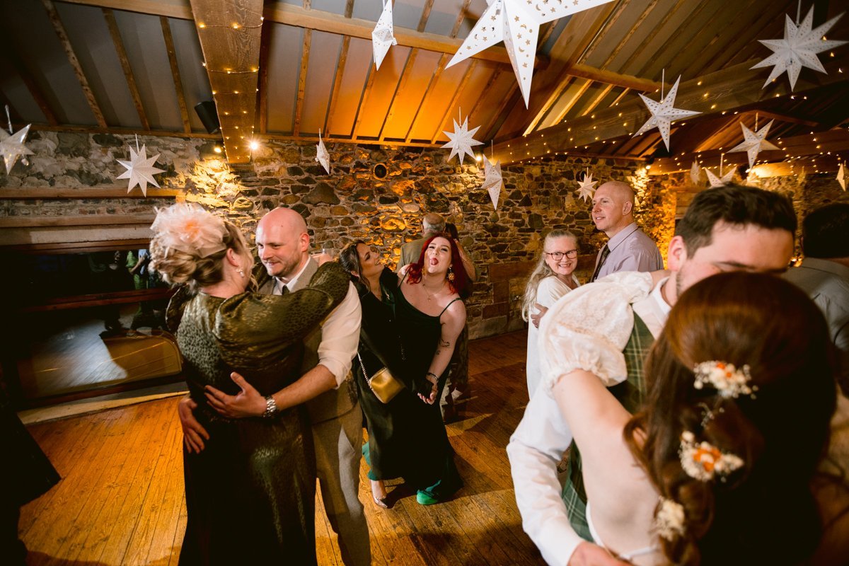 In a festively decorated room at Low Hall The Lakes, people are dancing and embracing under star-shaped paper lanterns and warm lighting, celebrating as if it were a small outdoor wedding.