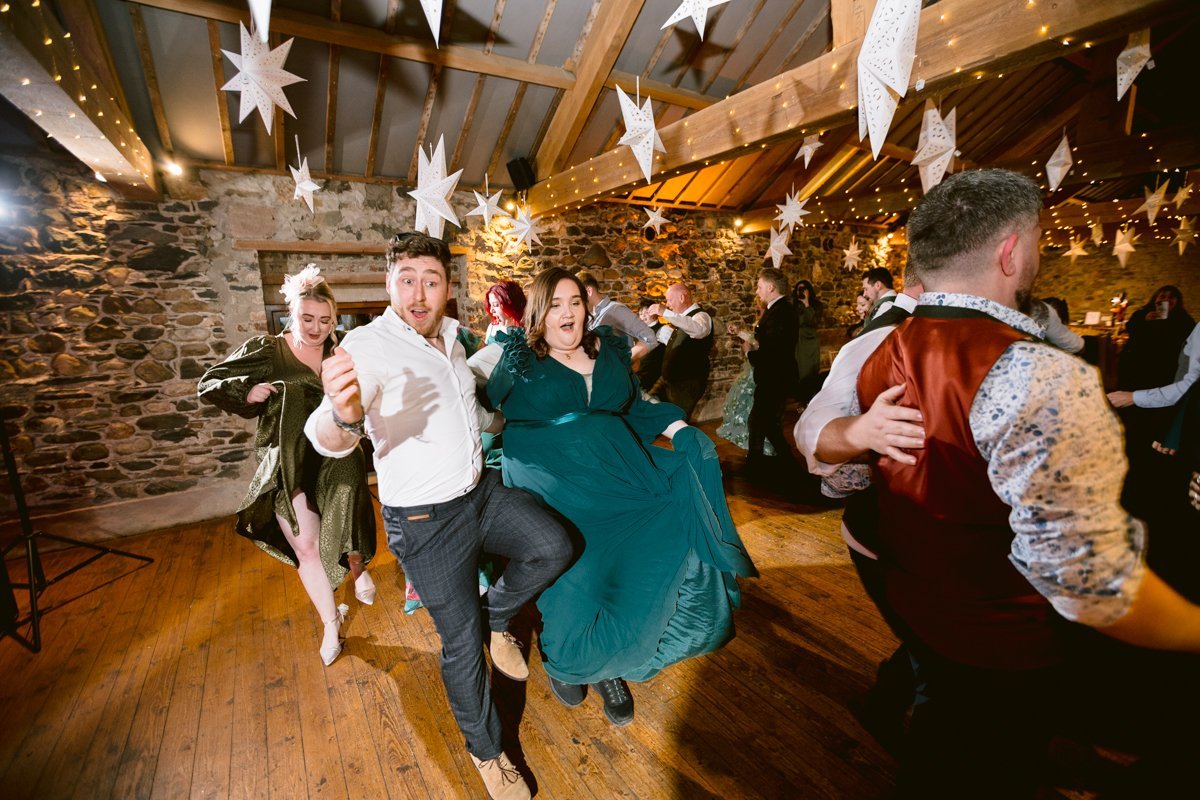 At Low Hall, people are energetically dancing in a rustic venue adorned with star decorations and string lights, celebrating a small outdoor wedding near The Lakes.