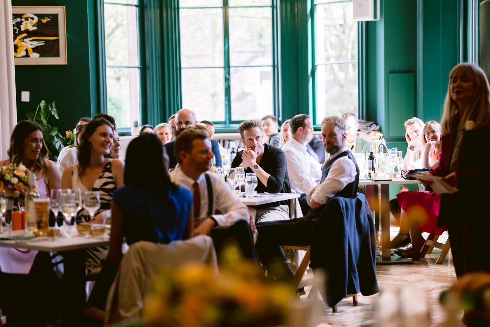 Guests seated at tables in a well-lit room at Tullie House, attentively listening to a woman speaking at the front—an ideal setting for a spring wedding or elegant wedding venue gathering.
