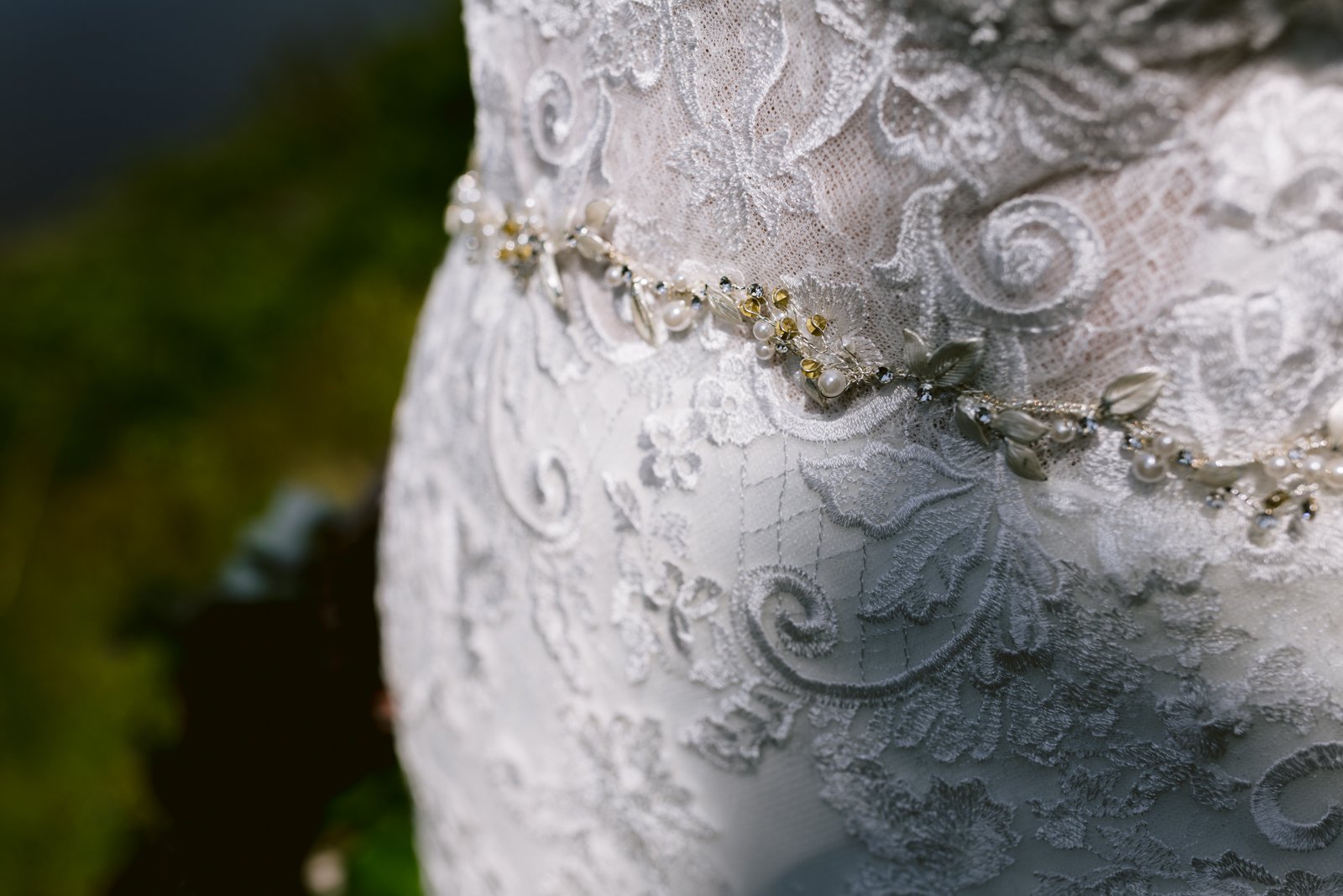 Close-up of a white lace wedding dress with a delicate beaded waistband, showing floral patterns and intricate details.