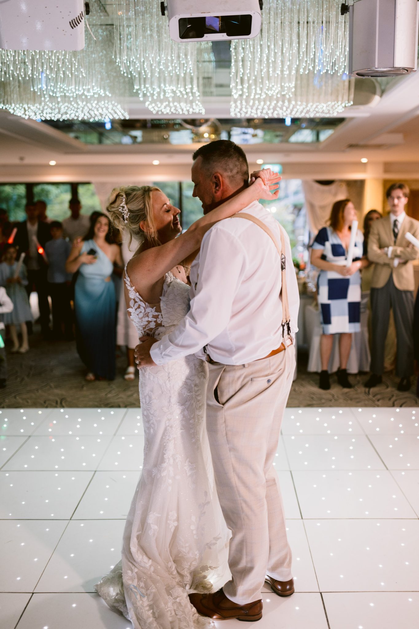 A bride and groom share their first dance on a lit dance floor at Armathwaite Hall, as wedding guests watch in the background during a romantic August summer wedding.