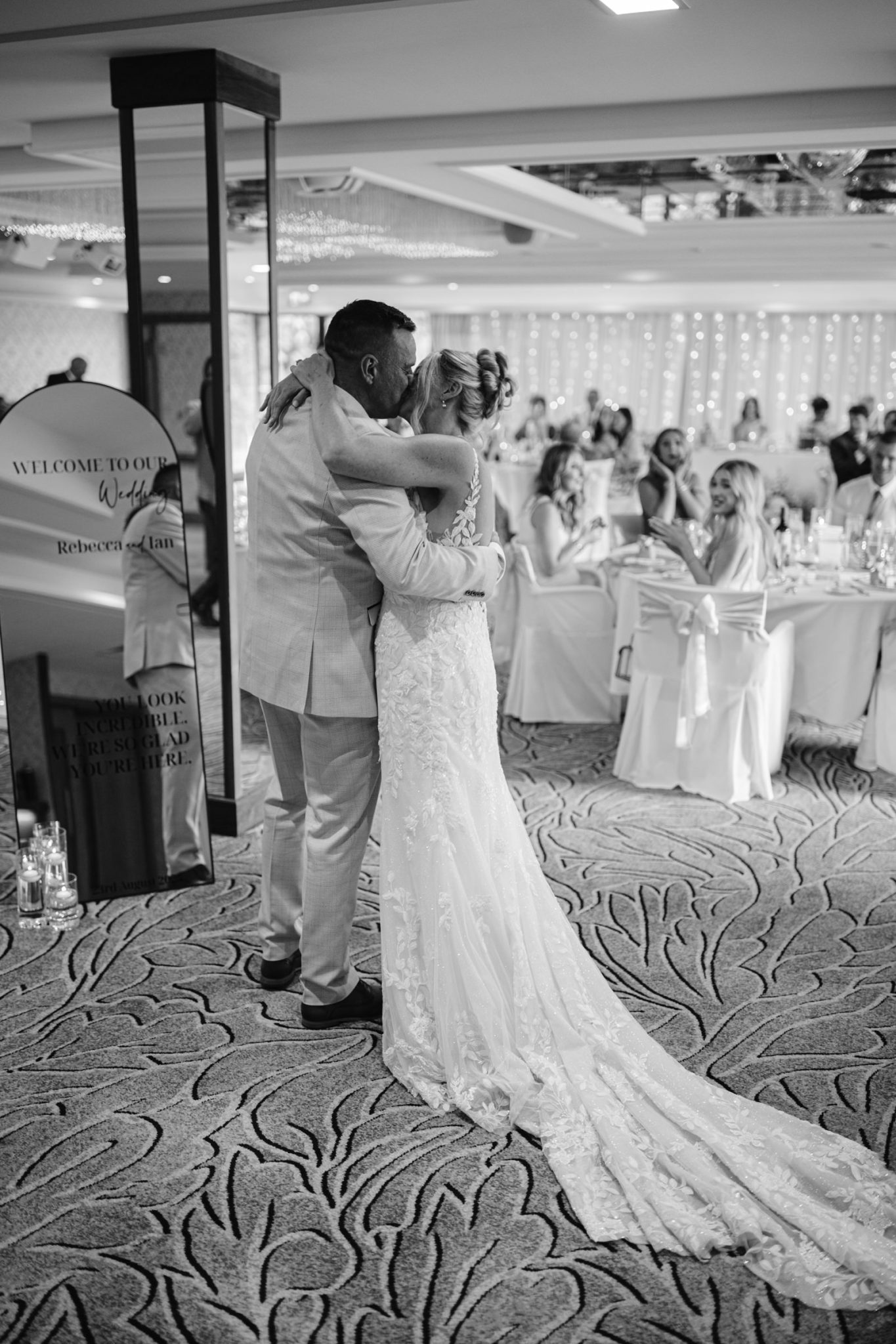 A bride and groom share a hug on the dance floor at their Armathwaite Hall wedding reception, surrounded by seated guests in a beautifully decorated indoor venue during an August Summer Wedding.