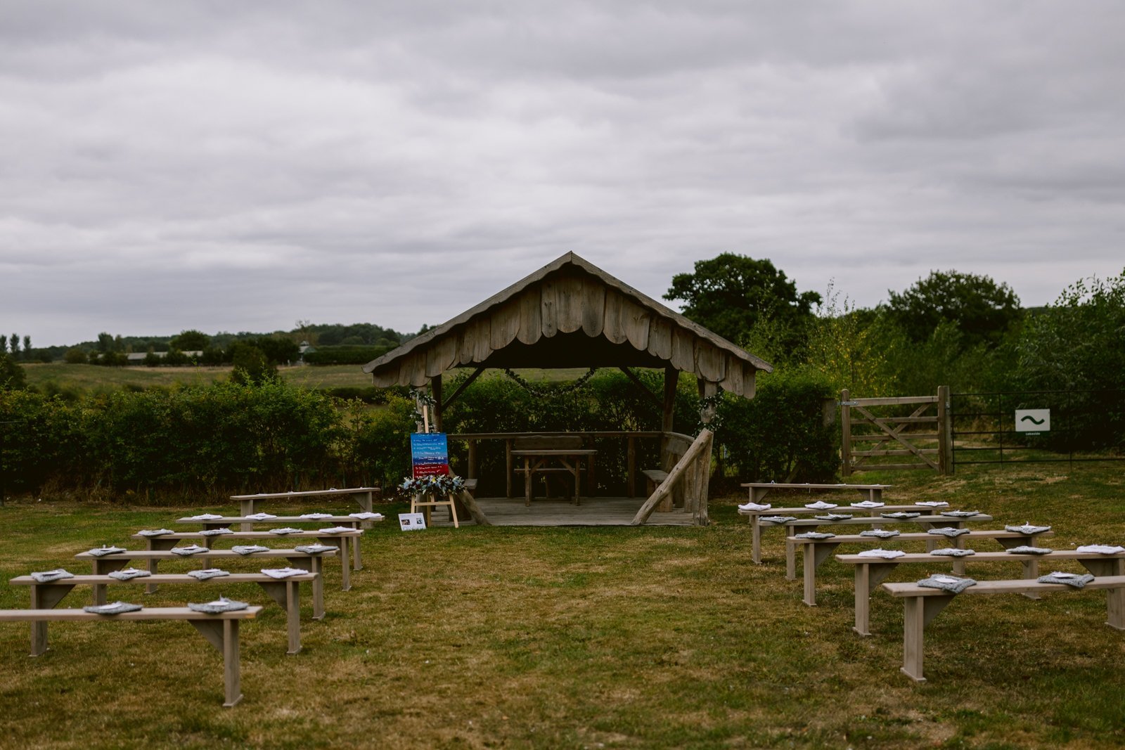 Outdoor wooden pavilion with rows of benches set on a grassy field under an overcast sky, perfect for a Rustic Farm Wedding in Shrewsbury. This venue is also proudly LGBT+ Friendly, welcoming all couples to celebrate their special day.