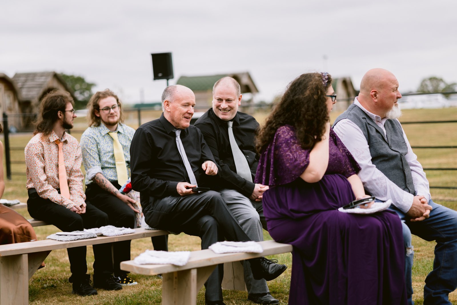 A group of people sitting on benches at a rustic farm wedding, enjoying the charming atmosphere near Shrewsbury.