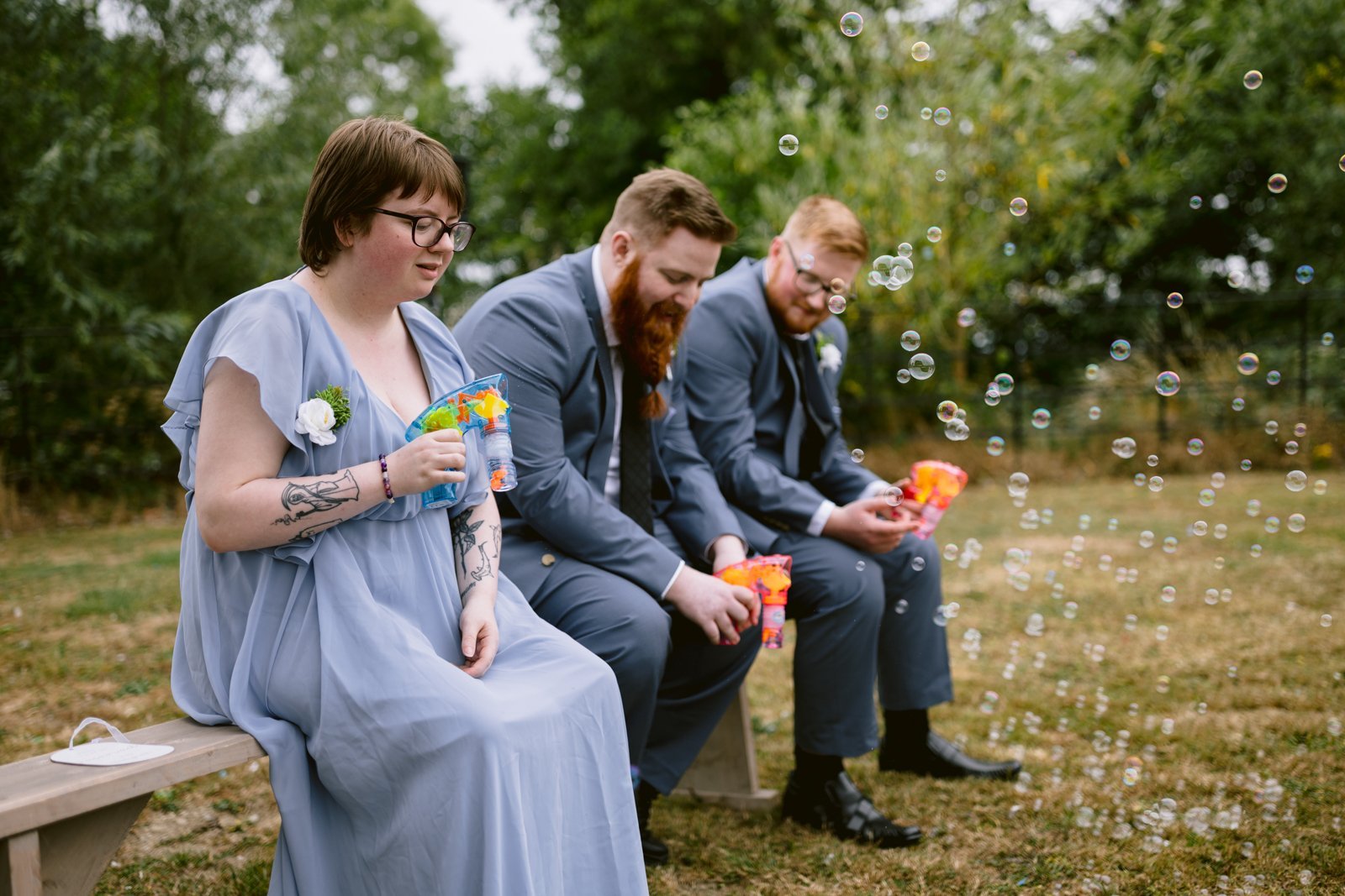 A group of people sitting on a bench with bubbles at a rustic farm wedding.