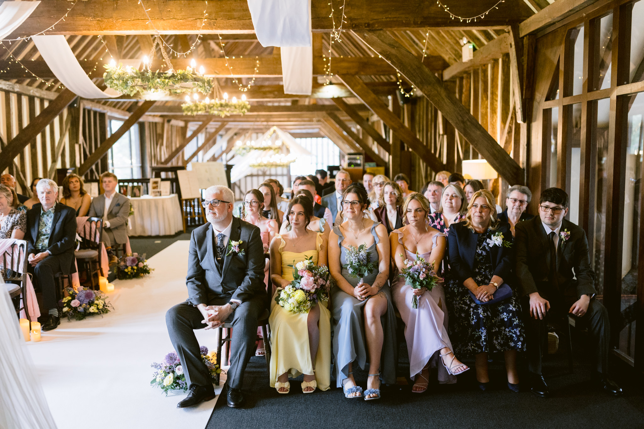 A wedding ceremony at Essendon Country Club in Hertfordshire, with guests seated in rows under rustic wooden beams and hanging fairy lights—perfect for unforgettable wedding photography.