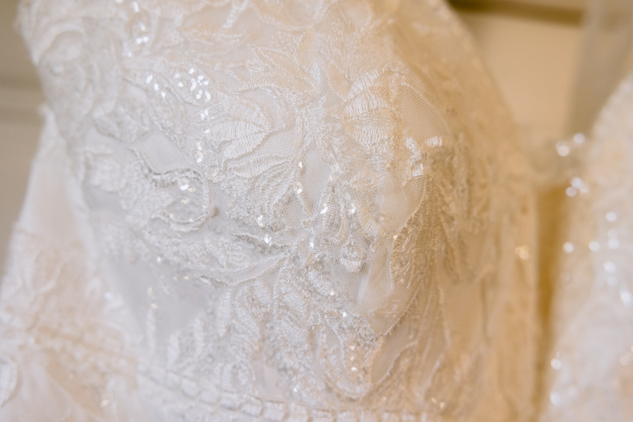 Close-up of the bodice of a white lace wedding dress with intricate floral patterns and subtle sequin detailing, beautifully captured in Upwaltham Barns Wedding Photography.