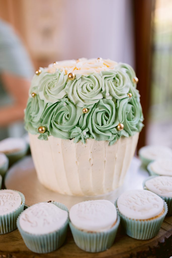 A large cupcake-shaped cake decorated with green rosette icing and gold pearls, surrounded by white iced cupcakes in blue cases—perfect for an elegant Upwaltham Barns Wedding Photography showcase.