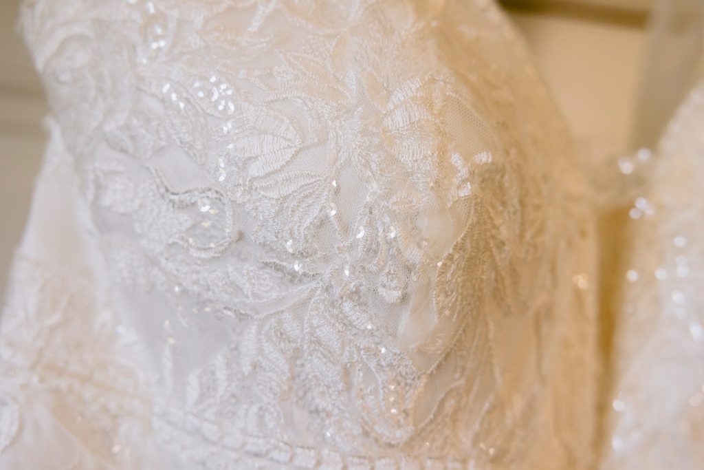 Close-up of a white lace wedding dress bodice with intricate floral patterns and subtle sequin details, beautifully captured as part of Upwaltham Barns Wedding Photography.