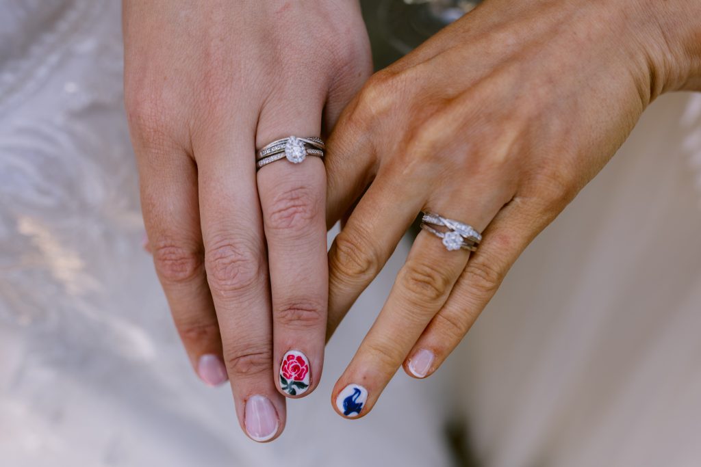 Two hands with wedding rings rest side by side; one has a rose painted on the nail, the other a blue lightning bolt design—capturing unique moments in Upwaltham Barns Wedding Photography.