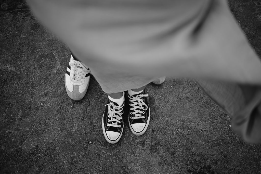 Black and white photo showing two people standing close together on a rough surface at Curbar Edge, each wearing different trainers.