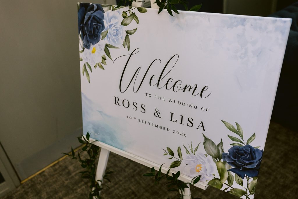 Wedding welcome sign on an easel, decorated with blue and white flowers, reads: “Welcome to the wedding of Ross & Lisa, 10th September 2026.” The perfect finishing touch for a Late Summer Wedding at The Maynard near Padley Gorge.