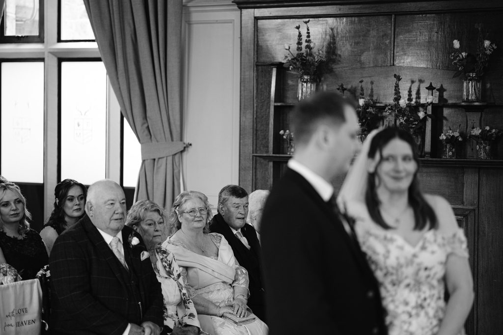 A late summer wedding unfolds at The Maynard, with seated guests watching a couple at the altar; the image is in black and white, capturing the timeless elegance of this Padley Gorge celebration.