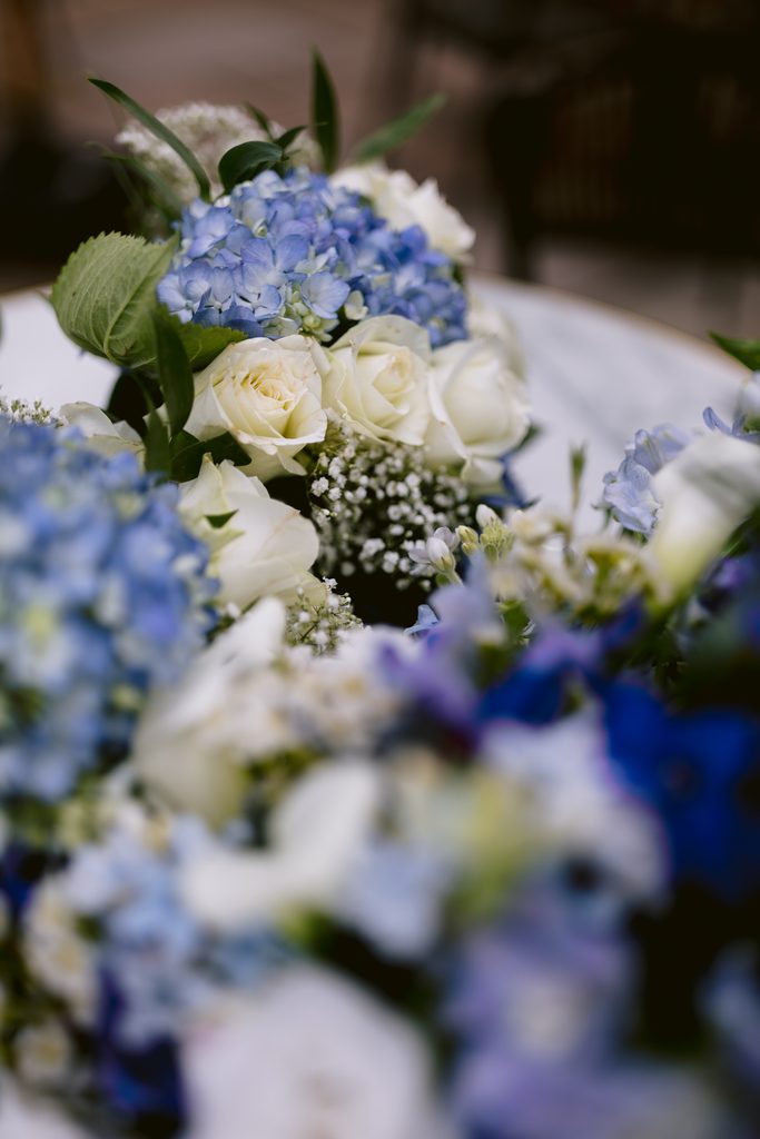 A close-up of a floral arrangement featuring white roses, blue hydrangeas, and baby's breath, with a blurred background—perfectly capturing the romantic ambience of a Late Summer Wedding at The Maynard.
