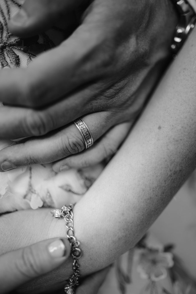 Black and white close-up of two hands touching; one hand wears a ring with engraved text and the other has a bracelet, capturing an intimate moment from a Late Summer Wedding at Padley Gorge.